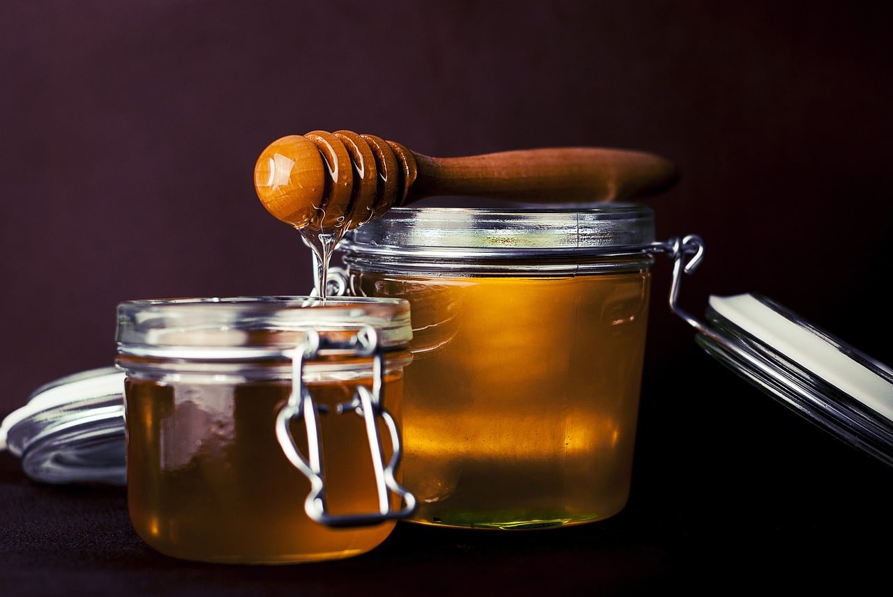 2 jars of honey with honey drizzler resting on top.