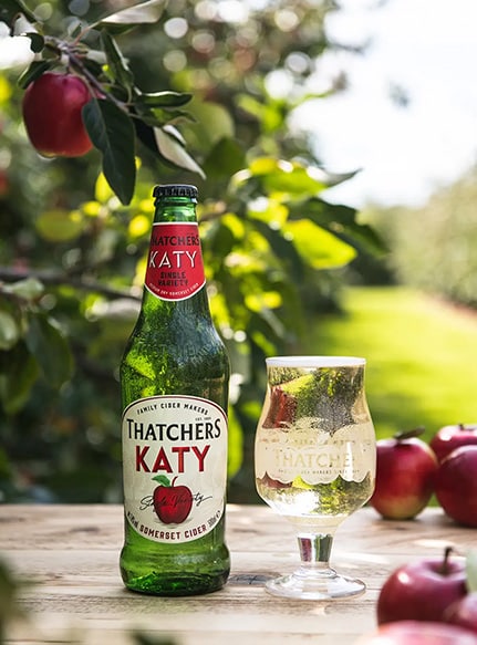 Green Thatchers cider bottle on a table in front of an apple tree.