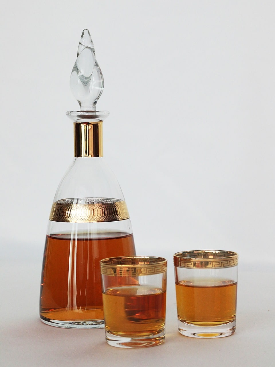 Elegant decanter and two glasses filled with amber-coloured liquor, adorned with gold accents.