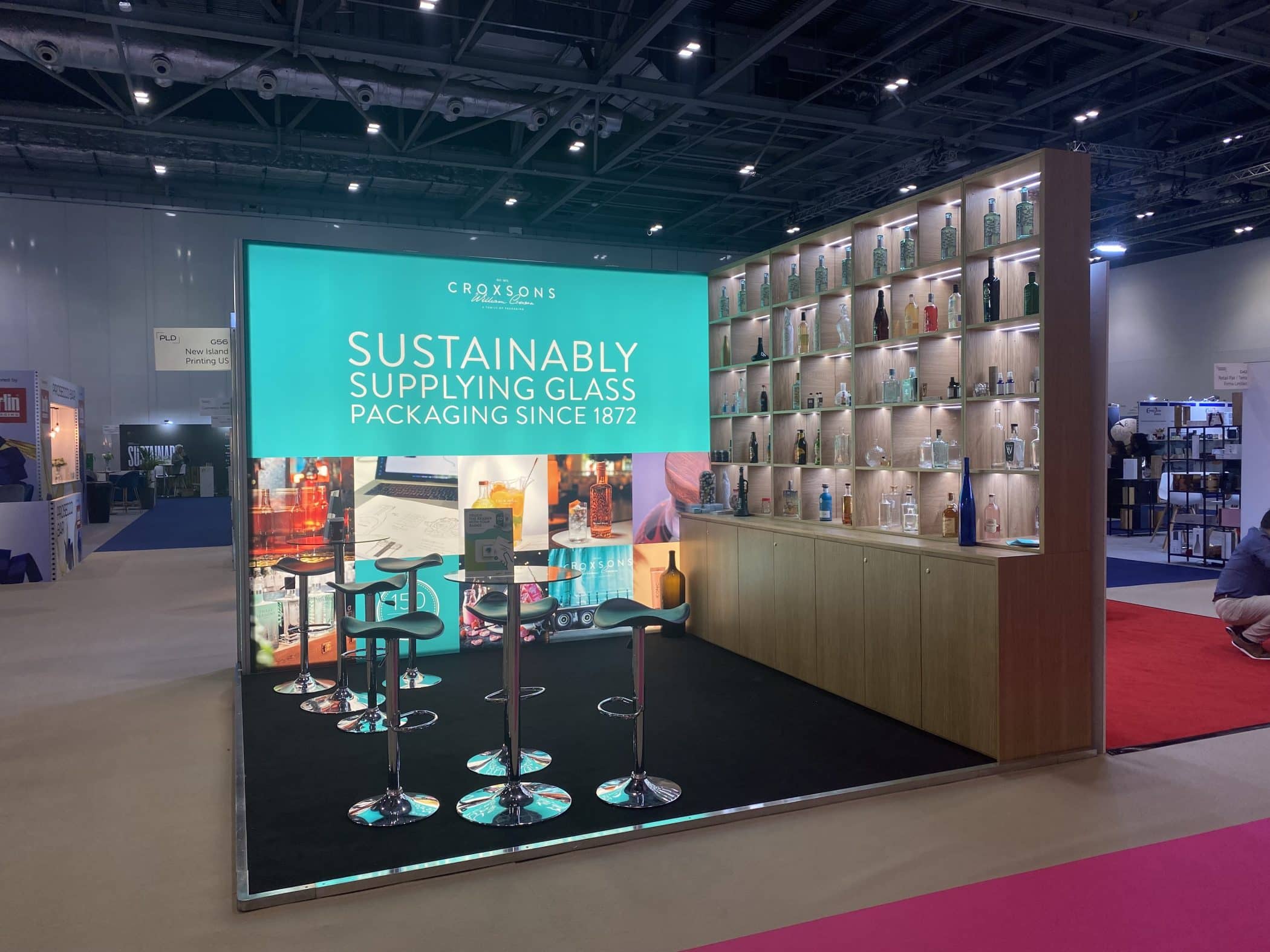 Exhibition stand with the worlds 'Sustainably Supplying Glass packaging since 1872' on one side and a bar set up.